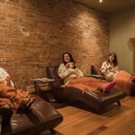 Three guests in robes sitting on brown lounge chairs in relaxation lounge